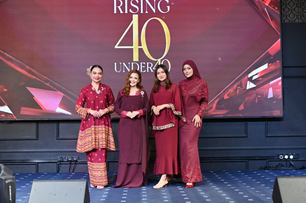 Four women in elegant red dresses posing on stage with the Rising 40 Under 40 campaign screen in the background