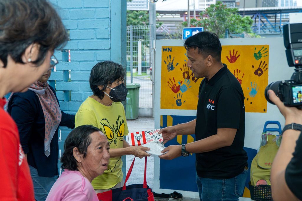 A KFC Malaysia volunteer distributing face masks and meal packs to vulnerable individuals during a community outreach session