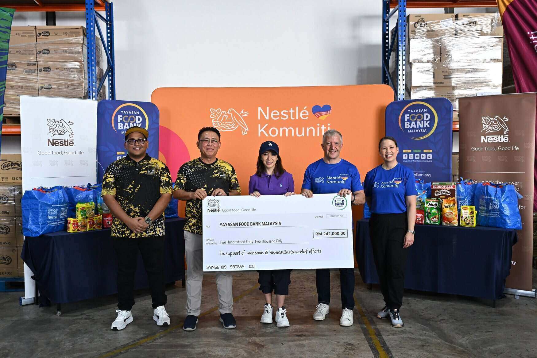 Wakil pengurusan Nestlé Malaysia dan Yayasan Food Bank Malaysia memegang replika cek RM242,000 di hadapan timbunan kotak makanan