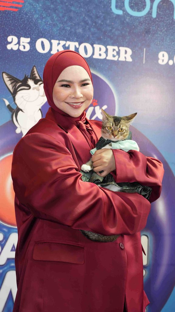 Penyanyi Aina Abdul berbaju merah hati tersenyum sambil memangku kucingnya Oked yang memakai baju kemeja di acara Cat Fashion Week