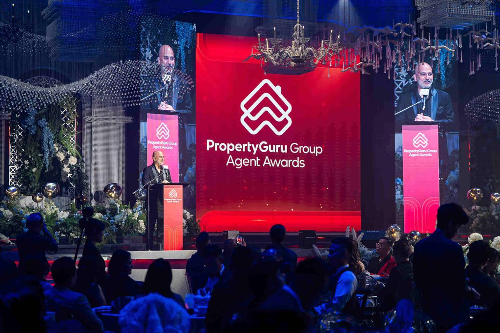 Barisan penerima anugerah memegang trofi bergambar bersama di atas pentas PropertyGuru Group Agent Awards berlatar logo merah