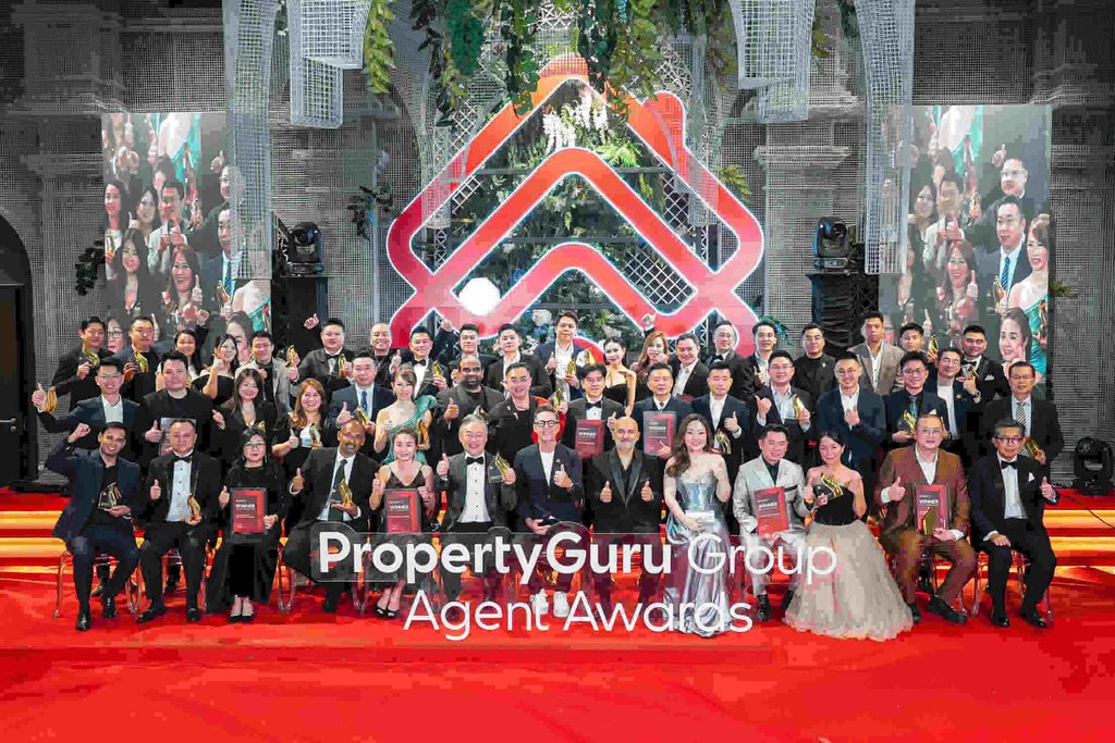 Barisan penerima anugerah memegang trofi bergambar bersama di atas pentas PropertyGuru Group Agent Awards berlatar logo merah